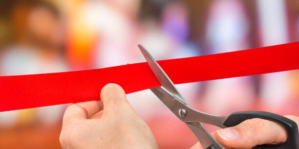Hand with scissors cutting red ribbon – opening ceremony concept