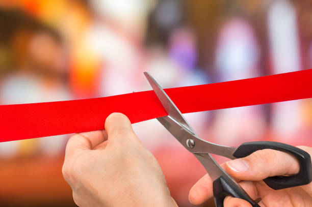 Hand with scissors cutting red ribbon – opening ceremony concept